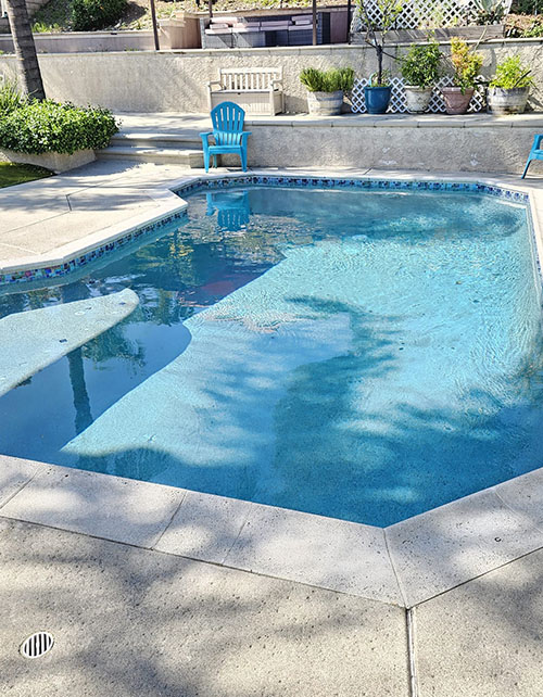 A serene pool scene featuring a blue chair and a blue umbrella