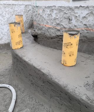 A concrete wall featuring yellow pipes and a hose