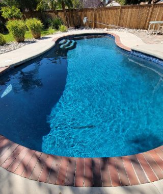 A serene pool featuring a blue tiled floor, surrounded by a charming brick patio