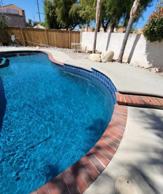 A serene backyard pool surrounded by a fence and a sturdy brick wall