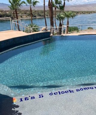 A serene pool scene featuring a sign that reads, "It's 5 o'clock somewhere"