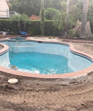 A backyard under construction featuring a pool and a newly laid brick patio