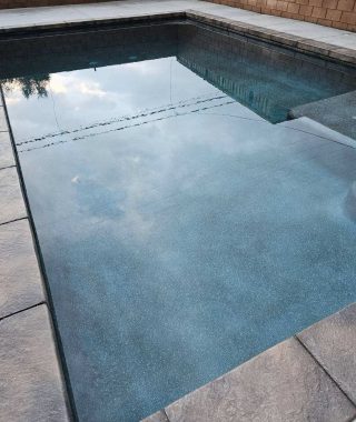 A serene pool featuring a sturdy concrete wall and a practical concrete step for easy access.