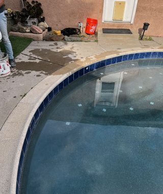 A man cleans a pool using a hose, actively working to keep the pool area pristine and ready for use.