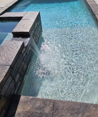 A person stands by a pool, admiring a beautiful water feature that enhances the serene atmosphere.