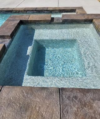 A serene pool surrounded by a stone patio, featuring a relaxing hot tub for leisure and enjoyment.