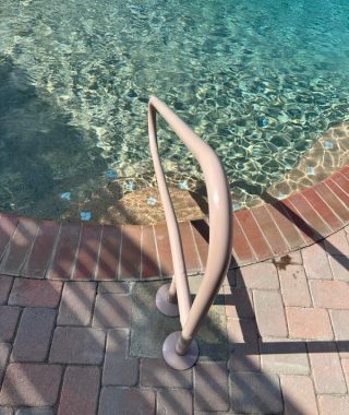 A handrail positioned at the edge of a pool, providing safety and support for individuals entering or exiting the water.