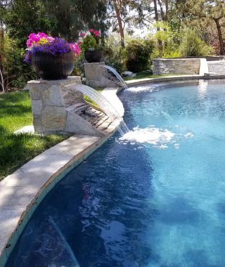 A serene pool featuring a cascading waterfall, surrounded by lush greenery, creating a tranquil outdoor oasis.